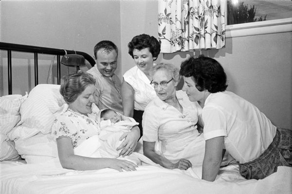 Gary Corcoran Jr., a newborn in the arms of his mother, Lois, with his father and three neighbors looking on. The baby was born at the home of Mr. and Mrs. B.E. Hogoboom, 1302 MacArthur Road, attended by Mrs. (Sarah) Hogoboom, right, and Mrs. Jack Salter, center, 3 Downer Circle. Mrs. Willard (Norma) Ryan, 1225 MacArthur Road, second from right was alerted for help by Gary Corcoran, Sr., 1213 MacArthur Road.