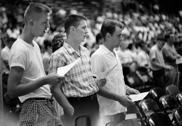 Three U.W. freshman (foreground) singing university songs during the freshman orientation in the field house.