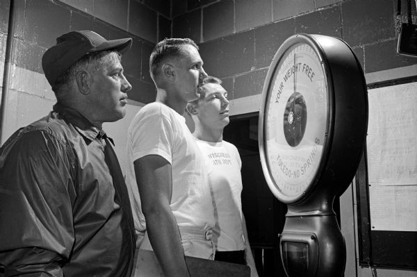 University of Wisconsin football coach Milt Bruhn watches as two of his players weigh in. Bill Smith (center) is the lightest on the team at 155 pounds. Pat Richter (right) is the tallest and one of the heaviest at 229.