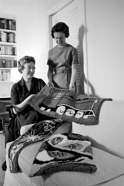 Mrs. Jerome Schwartzbaum (left) and Gertrude Kimbrough look at decorative hookings made by members of the handicrafts group of the Junior Division of the University League.