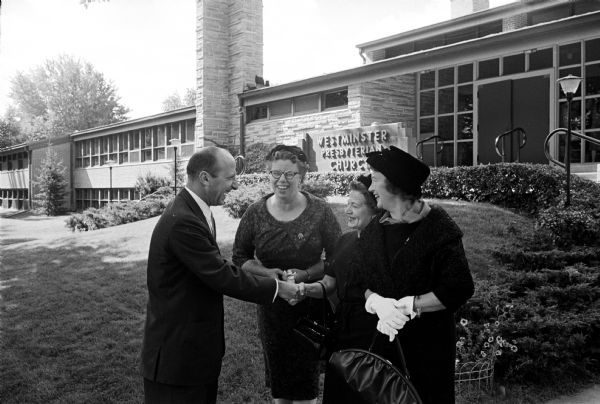 Dr. Leslie H. Fishel, Jr., director of the Wisconsin State Historical Society and guest speaker at the tea, sharing a laugh with three of the league members. The three women are Cristina Dana, Lenore Bainbridge, and Margaret Weyrough. Behind them on an outside wall are the words: "Westminster Presbyterian Church" in raised letters.