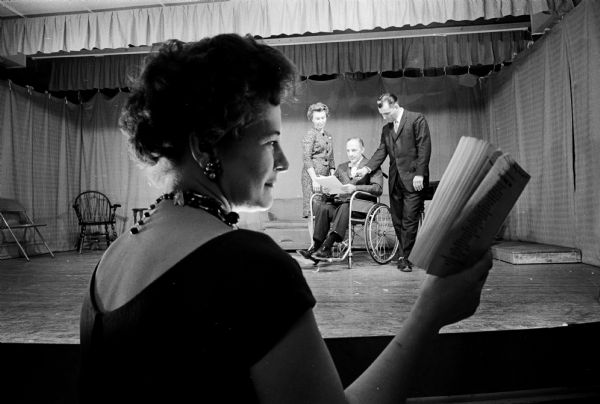 Four members of the St. James Players rehearsing for their play, "Lo and Behold!" Shown in profile in the foreground looking at a script is the prompter Dorothy Jafferis. Behind her, on stage are Nelda Roemer; Tom Jafferis, who is sitting in a wheelchair; and Richard Roemer.