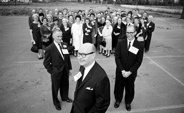 A scene from the annual Wisconsin State Journal correspondents' conference showing editorial staff members standing in front of a large group of mostly female local correspondents. Left to right: Harold McClelland, state editor; Lawrence Fitzpatrick, managing editor; and Steven Hopkins, assistant state editor.