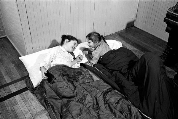 Betsy Silber and Ann Simmons are shown in lively conversation in their sleeping bags on the floor of the YWCA gym. Cold weather sent 49 girls inside for their camping experience.
