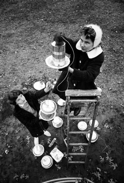 Janet Hirsch, 12, 601 Pickford Street, on a ladder, and Nan Newhall, 12, 4818 Woodburn Drive, seventh graders from Troop 33 at Cherokee Heights School, hanging bird feeders they made from fruit juice cans and pie plates.