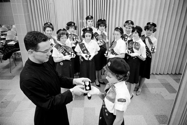 Girl scouts from St. Patrick's Catholic Grade School are the first in the Madison Diocese to receive the Marian Award, the highest Catholic scouting award. The Rev. Ronald Rank, spiritual adviser, presents the award to Eileen Allen, 1130 E. Mifflin St. Other St. Patrick girl scouts receiving the award are Sandra Lalley, 622 E. Mifflin St.; JoAnn Minter, 1139 E. Mifflin St.; Kathleen Mooney, 423 N. Ingersoll St.; Linda Niebuhr, 725 N. Powers Ave.; Susan Jordan, 1879 E. Main St.; Susan and Sandra Bass, 1965 Heath Ave.; Virginia Doucette, 520 E. Johnson St.; Sally Logue, 918 E. Mifflin St.; and Donna Kidder, 101 S. Franklin St.