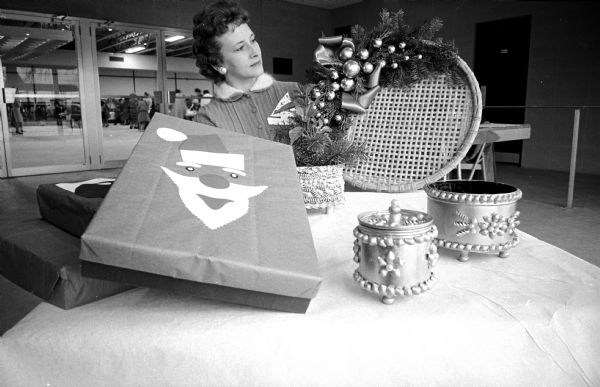 A member of Dane County Homemaker's Club displaying holiday decorations. Mrs. Delbert Bolleg, Mt. Horeb, admires a holiday cane tray, and decorated boxes, flower pots, and jars made from cans and embellished with macaroni.