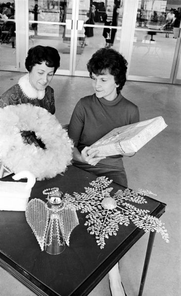 Members of Dane County Homemaker's Clubs displaying holiday decorations. Mrs. Gaylord Martinson (L) and Mrs. Arthur Sutter (R) of Mt. Horeb admire a wrapped box, a kitten box, a pilsner angel and snow flake decorations.