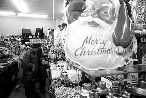 A family standing in an aisle looking at Christmas decorations. There is a large Santa Claus balloon is in the foreground.
