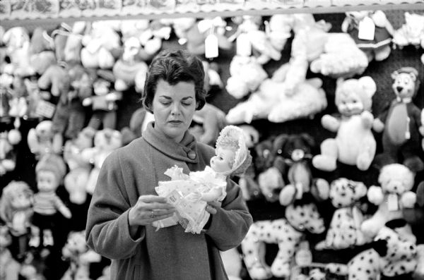 A woman is holding a doll while standing in front of a display of dolls and stuffed animals.