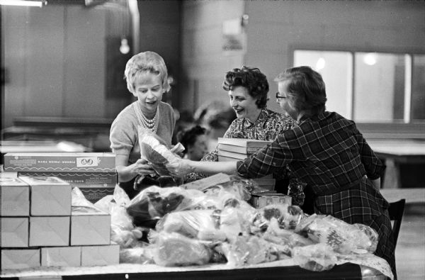 Wives of Wisconsin State Journal and Madison Newspapers, Inc. select gifts at the toy depot of the Empty Stocking Fund. From left to right are: Mrs. Edwn Stein, Mrs. Gordon Johnson, and Mrs. Howard McCaffrey.