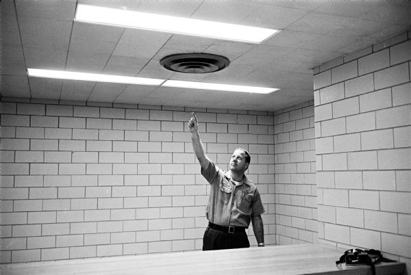 Jailer Max Koons pointing to the hastily-repaired ceiling in the lobby of the Dane County Jail which two inmates tried to claw open during an attempted escape. William Welter and Lawrence Nutley were in solitary confinement after being accused of slaying a policeman in Lake Delton in August.