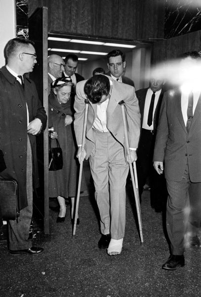 Accused police slayer Richard Nickl ducking photographers as spectators crowd the door to watch him leave Circuit Court. His left leg in cast was fractured when he fell from a getaway car. The bullet wound in his right leg has healed. William Welter, Lawrence Nutley, and Richard Nickl, all of the Chicago area, were accused of slaying Patrolman James Lantz, Baraboo, and the wounding of Lake Delton Police Chief Eaugene Lee Kohl in an early morning gun battle in front of the Lake Delton village hall.
