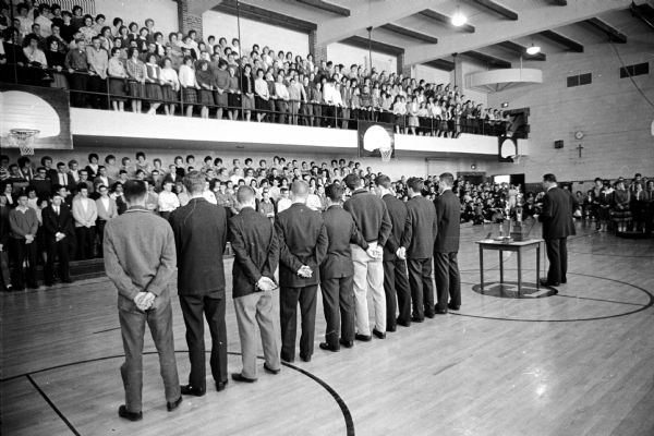Edgewood High School boys basketball team members and their coach, Dave Brown, are standing before the student body at a victory rally. They had won the state Catholic basketball championship.