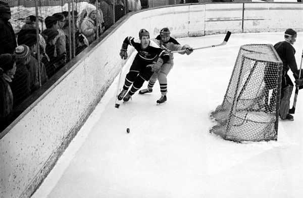 Action shot of a "Hawks" hockey player Tom Grumke skating through a check at boards to retrieve the puck before scoring.