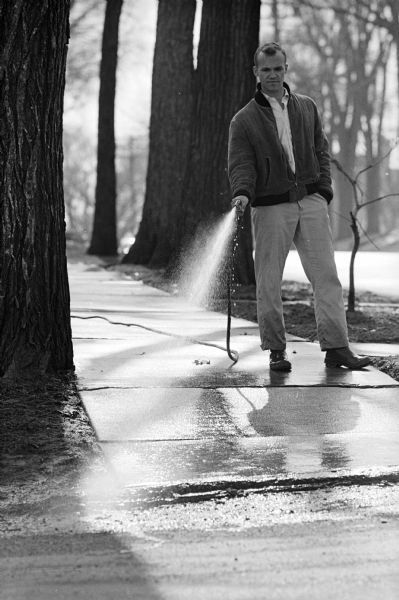 An unidentified man washing the sidewalk with a hose.