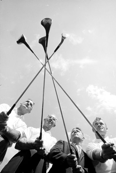 Four of the organizers of the Madison Service Clubs Olympics pointing their golf clubs high toward a record turnout for the 1962 event at the Monona Municipal Golf Course and the East Side Business Men's Club. Golf, badminton, darts, horseshoes, bait casting, volleyball, bridge, cribbage, euchre and checkers are listed as the events. Left to right are: Walter Engelke, Bob Widmer (chairman of the event), J.H. Cottrell, Jr., and James Schumacher.