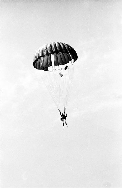Three experienced sky divers, Miles Micya and Mel Gall of the Air Force, and Bob Falconer (Falkener), a U.W. student, jumped into Lake Mendota from an airplane. Here a sky diver is opening the chute and then is slowly falling toward the lake.