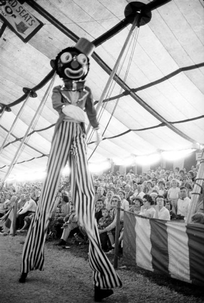 A circus clown on stilts is walking past the audience in the Big Top set up at the Dane County Fairgrounds.