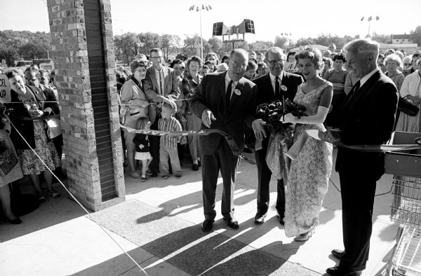 Miss Wisconsin, Joan Mary Engh, is cutting a symbolic ribbon signifying the official opening of the new A&P supermarket in the Hilldale Shopping Center. Assisting her are R.C. Redtke, vice president of A&P's Midwestern division, left, and Ralph Johnson, the store manager. The supermarket is the first business place to open in the shopping center.
