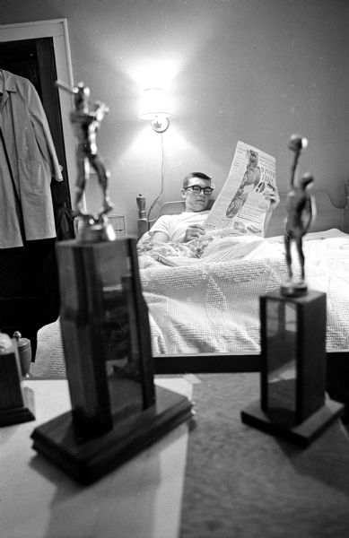 Pat Richter relaxing at home. Two trophies are in the foreground, one for baseball, the other for basketball. He is also an All-American football player.