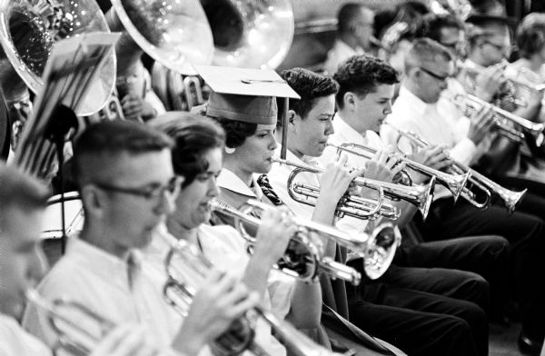 Close-up view of five trumpet players. Names (l to r) Norm Frater, Sandy Holdbrook, Marcia Ziebarth (wearing a graduation cap), Rick Moe and Ken Connor.<p>Marcia Ziebarth was graduating, but returned to the band to play, she was class of '63. Norm Frater, Sandy Holdbrook and Ken Connor were '64 and Rick Moe was '65. Rick was a first trumpet/cornet who played in the Madison Scouts.</p>
