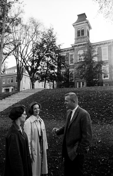 Thirty-one year old Dr. Evert Wallenfeldt, newly appointed president of Milton College, is shown chatting with two students in front of Main Hall. The students are Barbara Abbott and Patricia Barnes, both from Madison.