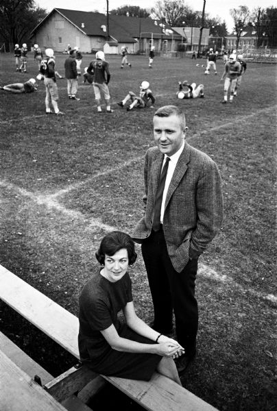 Milton College president Dr. Evert Wallenfeldt and his wife, Phyllis, are shown at the side of the Milton College football field, with practice going on in the background. Dr. Wallenfeldt is one of the youngest college presidents in the U.S.