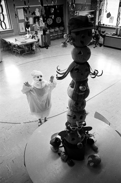 Teresa Vos, age 5, dressed as a ghost, pays homage to a pumpkin totem pole at Gompers school.