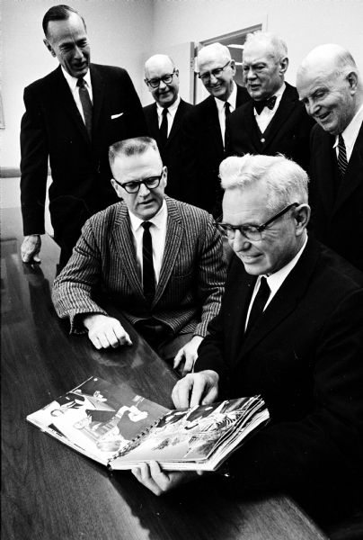 A photo book recording the visit of Oslo Norway's Mayor Rolf Stranger  is presented to Mayor Henry E. Reynolds (seated at right) by John Kreissler, Wisconsin State Journal photographer, who took the pictures. Looking on at the presentation are, left to right: Don Anderson, Lawrence Fitzpatrick, Melvin Reppen, Arthur Towell, and Basil Peterson.