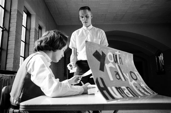 Barbara Mani, in the lobby of East High School, is shown registering Phil Farguharson for his participation in a youth rally on human rights to be held February 22. Similar registration tables were set up at Central, West, Monona Grove, Edgewood, and Wisconsin High Schools.