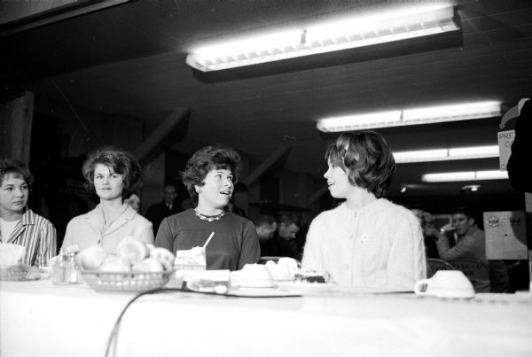 Judy Noble, 18, a Burlington High School senior, is named the 1964 Wisconsin Pork Queen at the Wisconsin Spring Market Hog Show banquet.  At the right is another queen candidate, Pat Yaeger of Fond du Lac.  The two women on the left are not identified and did not appear in the WSJ published photograph.