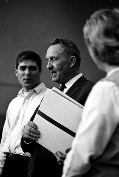During Wisconsin High School's last pep meeting, Principal John J. Goldgruber, center, smiles as he holds a memory book presented to him by students Charles Jacobsen and Nancy Johnson, standing on either side of him. At the end of the school year, Wisconsin High would be closing to merge with Central High School.  The memory book contained personal letters and poems from almost all of the school's 186 students.