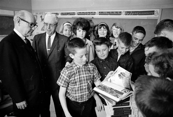 Children of St. Mary of the Lake school gather around as Lawrence Fitzpatrick (left), managing editor of the Wisconsin State Journal, presents a 20 volume World Book Encyclopedia to Darrell Henry, 12,(center) grand prize winner of the State Journal's Sunday Funland puzzle contest. Harry Bunbury, seventh grade teacher, is standing second from left.