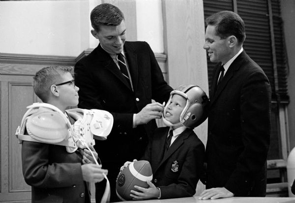 Washington Redskins end Pat Richter, second from left, is shown adjusting the helmet of John Haase, 10, as John's brother, Bill, 13, and the boys' father, Roy T. Haase, watch. Richter, a former University of Wisconsin athletic great, will be on the program of the Bethel Lutheran Brotherhood fathers and sons sports banquet, along with other professional football players.