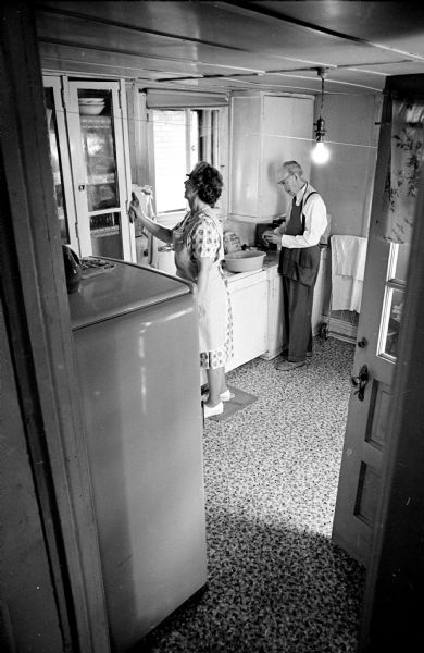Marie Ackley gives the kitchen of Mr. and Mrs. Alfred Lund a woman's touch while Mr. Ackley prepares dinner. Mrs. Ackley works as a health aide in a new Visiting Nurse Service program.