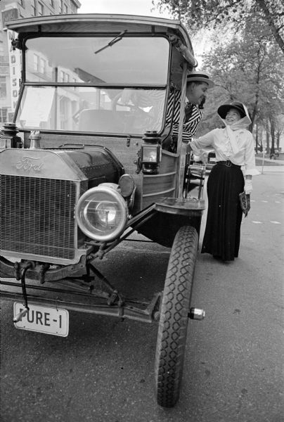 Man and woman in costume (he is in the driver's seat and she is standing) beside an "antique" truck. On the side is a sign (not visible) that reads "Miami to Minneapolis, Pure Oil Co."