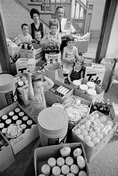 William Coughlin, winner of an A & P supermarket shopping spree, with his wife Barbara and their seven children posing in their living room with the $998 worth of groceries he was able to carry out of the supermarket in 15 minutes. The groceries included 96 lbs. of peanut butter, 50 tubes of toothpaste, 150 lbs. of laundry detergent, 10 turkeys and 20 cans of hair spray.