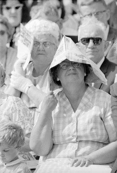 Woman spectator sitting at the commencement ceremony inside Camp Randall stadium wearing an "improvised sun bonnet" made of folded newspaper.