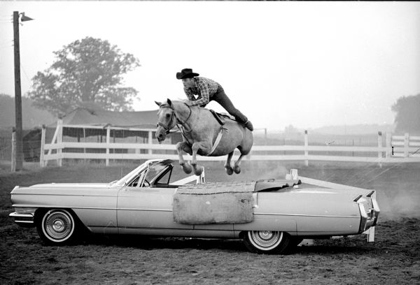 Stuntman Butch Rivers jumping his horse over a car to demonstrate some of the features in store for spectators at the World's Championship Rodeo which will be held at Holmes No-Oak Ranch on Syene Road. Proceeds from the rodeo go to the Wisconsin State Journal Empty Stocking Club and the Capital Times Kiddie camp.
