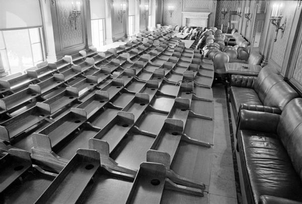 The desks and chairs of the state assemblymen are shown stored in the Assembly lounge while the Assembly chamber is recarpeted. Over a four-year period that started in 1961 the state Building Commission has spent $1.2 million for converting the Capitol's electrical system from direct current to alternating current.