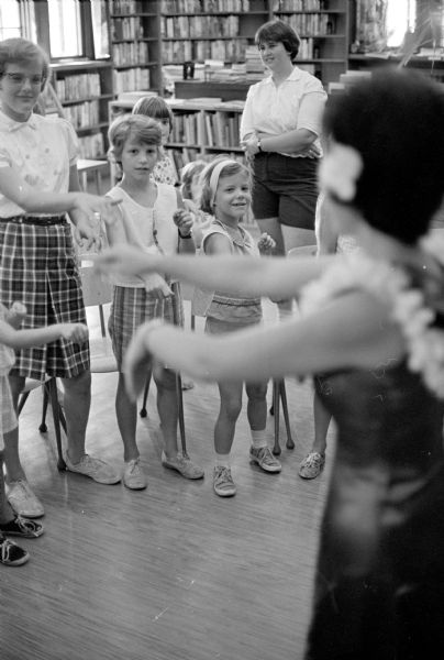 Joan Nagamatsu, 2110 University Avenue, a native of Hawaii, illustrating hula movements to a group of young children at the Madison Public Library, 206 North Carroll Street.
