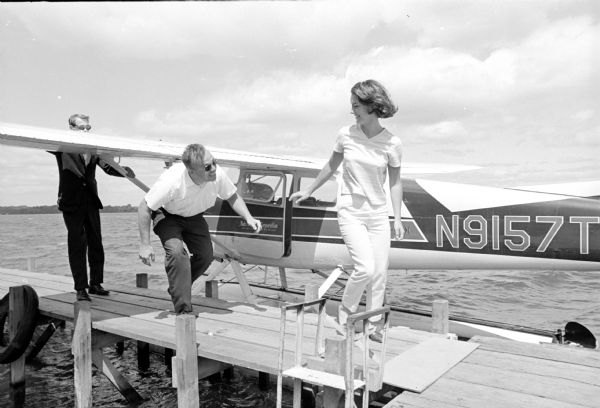 Miss Madison, Abbie DeBuhr, stepping from a seaplane to the Memorial Union pier after a flight and cruise as guest of the Mohs Seaplane Corp. Burce Mohs, left, flew the seaplane. The plane ride was one of the Miss Madison contest prizes.