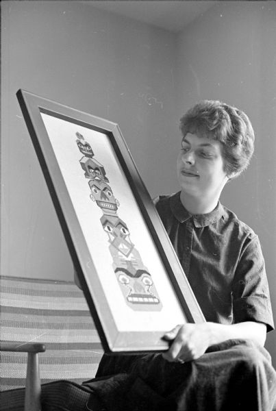 Elinor Schnore with her counted thread embroidery of a totem pole mounted in a frame.