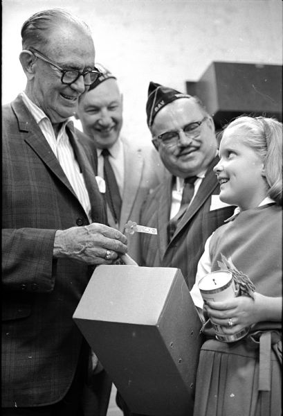 Wisconsin State Journal columnist Joseph (Roundy) Coughlin receiving an advance forget-me-not from Disabled American Veterans salesmen before the annual sale on Capitol Square. Salesmen, left to right, are Edwin (Spike) Carlson, general chairman and senior vice-commander; and Don L. Herlitz, commander, with his daughter Mary Lou.
