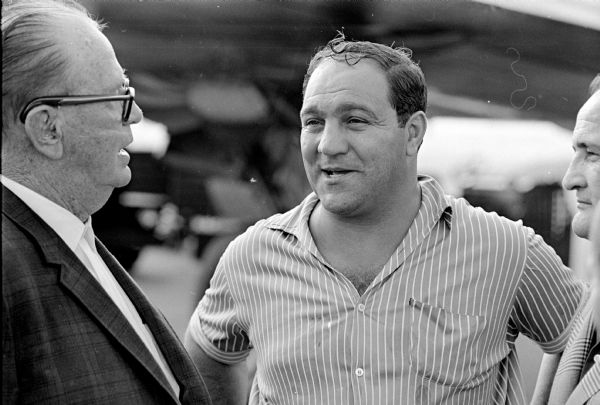 Rocky Marciano, retired undefeated heavy weight boxing champion, arrived in Madison for a day or two of rest. He is grinning as he is getting ready to shake hands with Roundy Coughlin, the Sage of Mendota. The photographs that appeared in the Wisconsin State Journal did not include Coughlin.