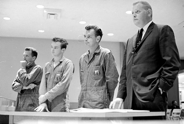 Three men arraigned in Judge William L. Buenzli's court on charges stemming from an armed robbery at the Edgewater Hotel stand with deputy District Attorney Donald McCallum, right. Richard Eickhoff, left, asked for a mental examination and a county-paid attorney, while Jerome Malinski, second from the left, and John Jacobs both pleaded guilty.