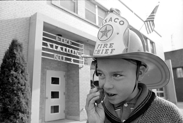 Jerry Hauser, 10, son of Fireman Michael and Barbara Hauser, is shown wearing a fireman's helmet equipped with a microphone and loudspeaker.  An open house was held at all Madison fire stations on Sunday, Oct. 4, and at each one a lucky child was to receive one of the battery powered helmets. This image was taken in front of Fire Station Number 3 on Williamson Street.