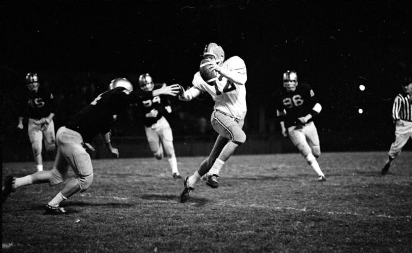 Madison East High School quarterback Bob Boyle eludes a Madison West defender to complete a pass to teammate Don Taylor down field. Craig Nobis of Madison West is chasing from behind.