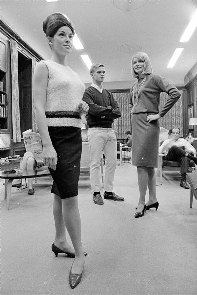 Three students in modeling poses. The Associated Women Students of the University of Wisconsin presented its annual fashion show in Great Hall.  The students are Vicki Morris, with foot turned and hair up; John Cloninger, with arms folded; and Toni Walter, with hands on hips.